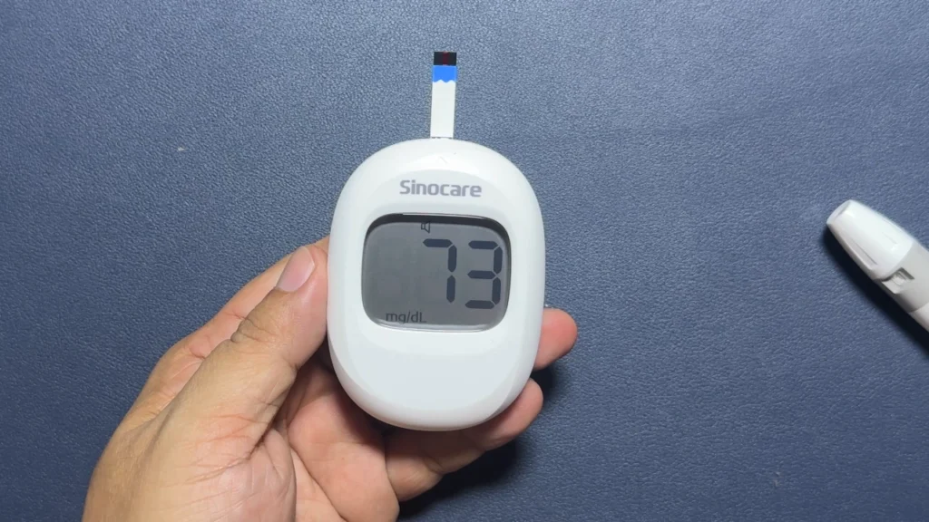 Hand holding a Sinocare blood glucose meter showing 73 mg/dL.