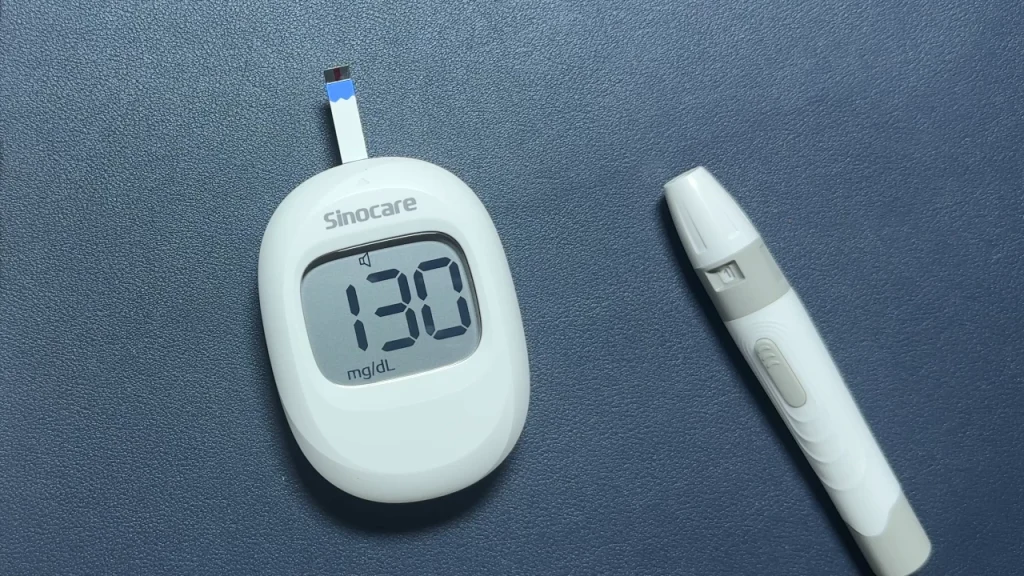Sinocare blood glucose meter showing 130 mg/dL beside a lancing device.